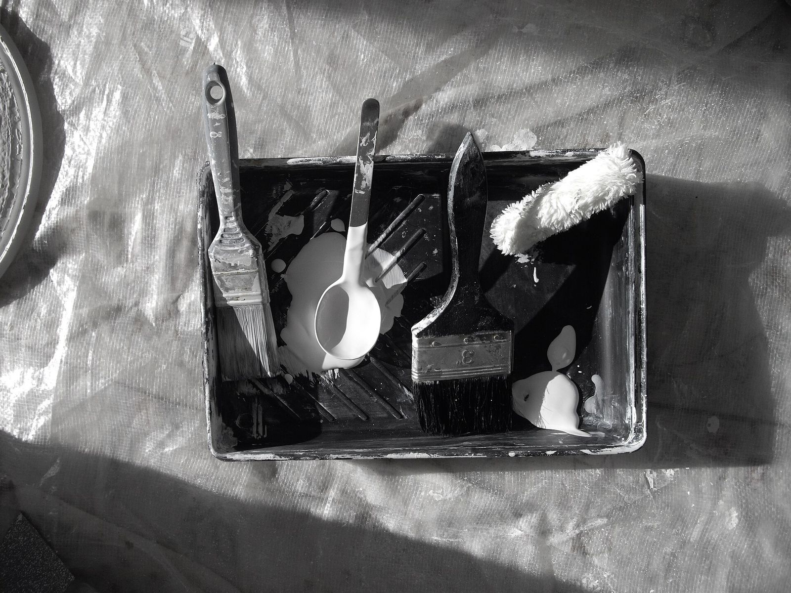 Paint brushes, a roller cover and a paint tray on a dust sheet