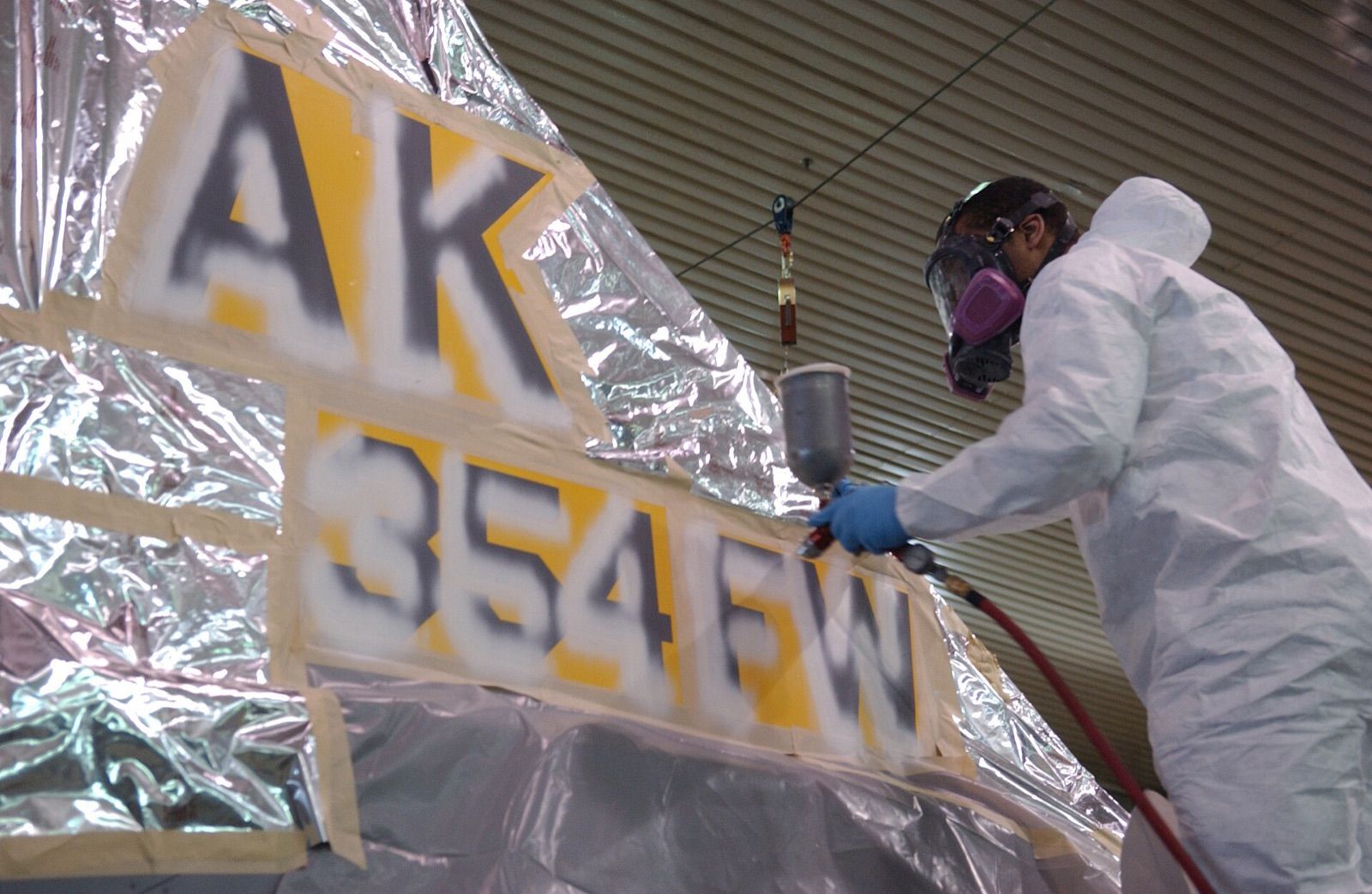 A painter in a protective suit and respirator using an HVLP spray gun on a masked panel