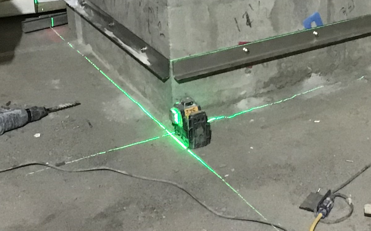 A green cross-line laser projecting level and plumb lines on a construction site