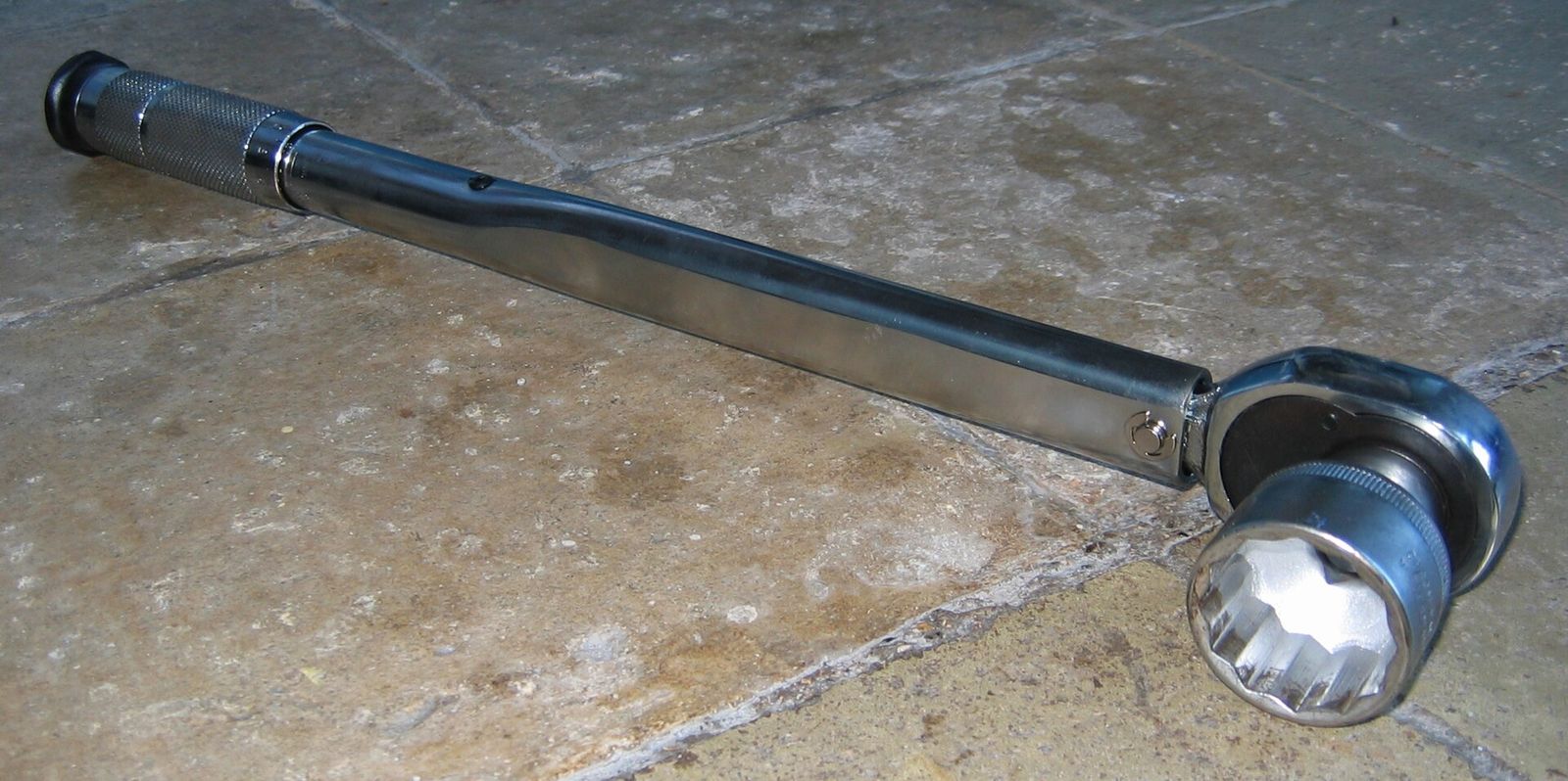 A long click-type torque wrench with a large socket fitted, lying on a concrete floor