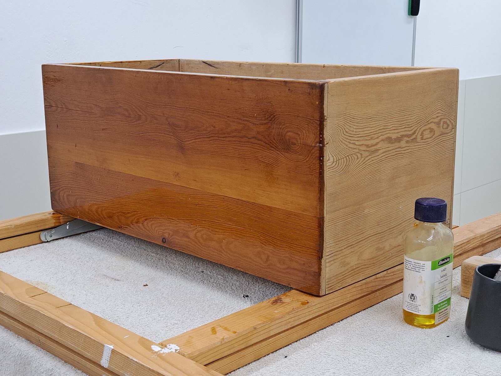 A pine box half finished with linseed oil, the oiled side darker and glossier than the bare wood