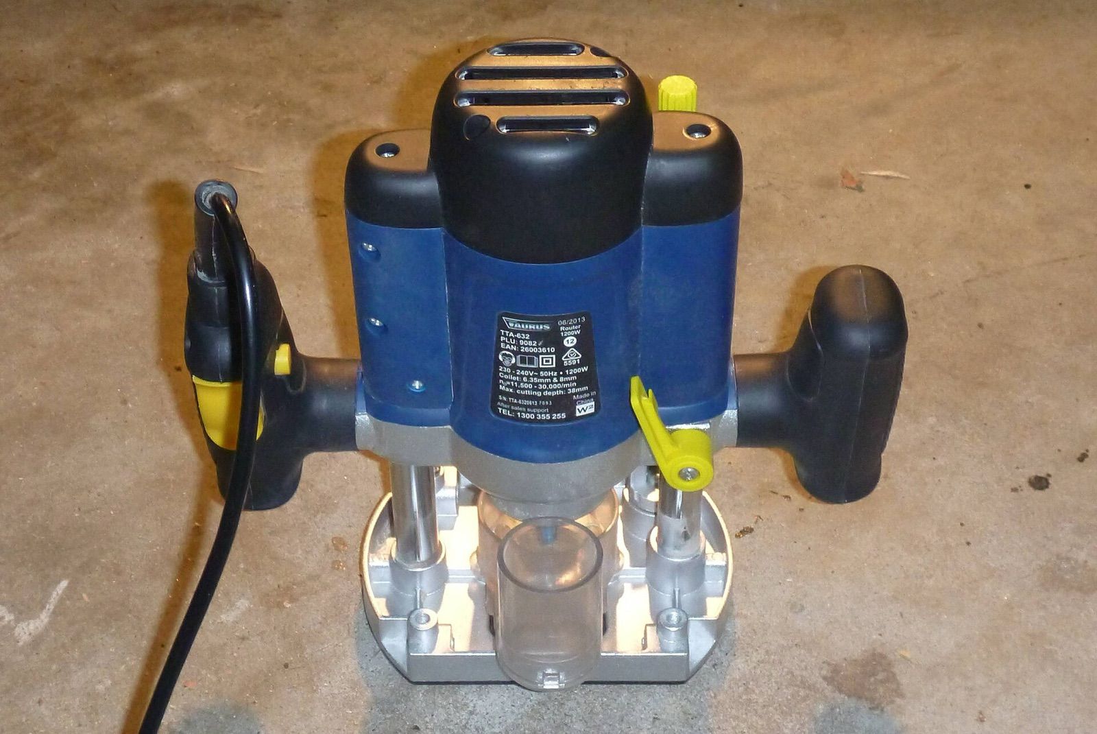 A plunge router with twin handles and a dust extraction port standing on a workshop floor