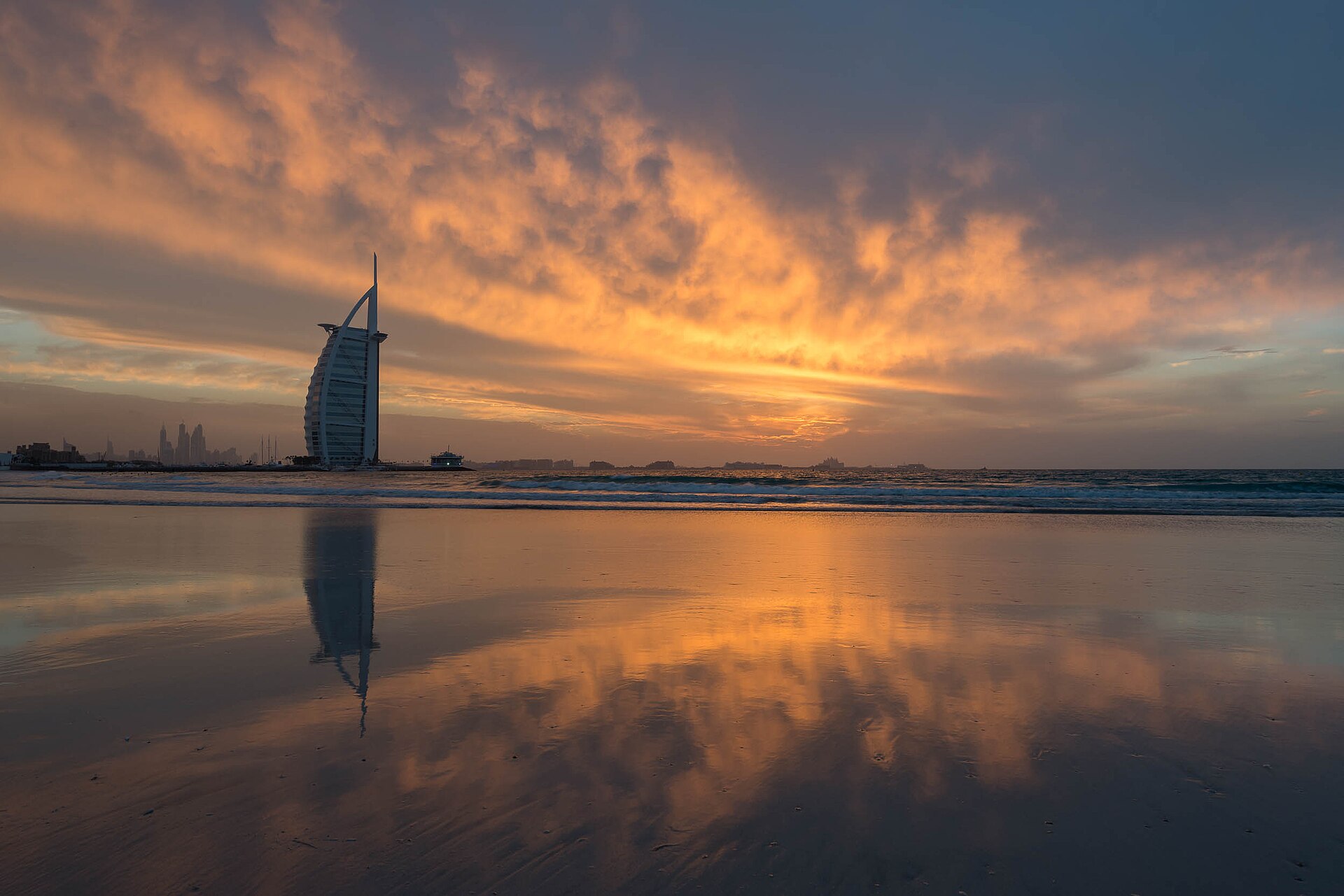 The sail-shaped Burj Al Arab silhouetted at sunset and reflected on the wet sand of Jumeirah Beach