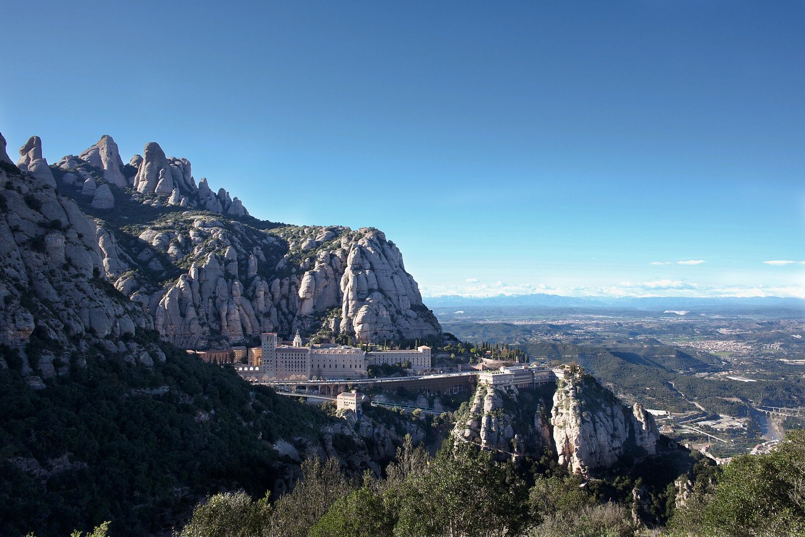The Montserrat monastery below the jagged rock pinnacles of Montserrat mountain, with the plains of Catalonia beyond