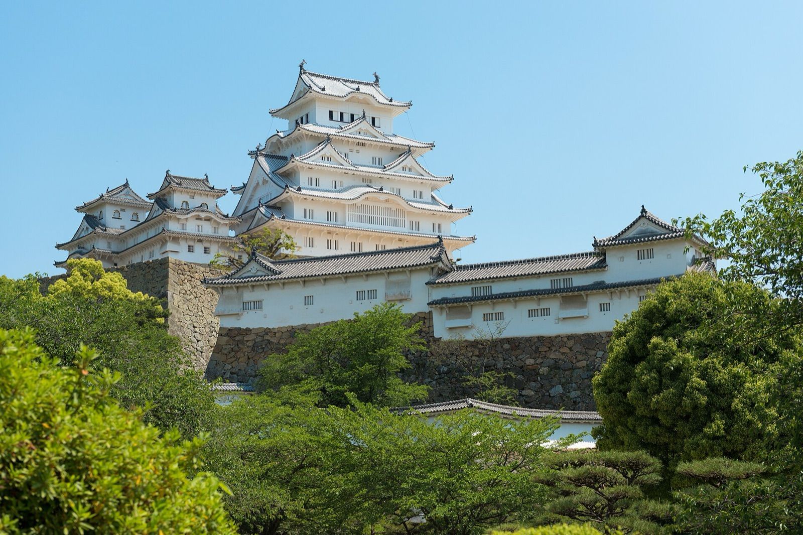 The white keep of Himeji Castle rising above green trees and stone walls