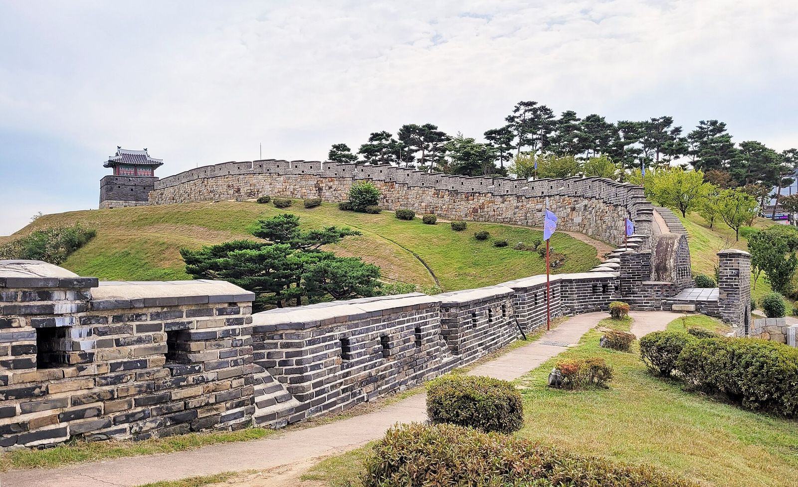 The stone walls of Hwaseong Fortress in Suwon curving over a green hillside towards a watchtower