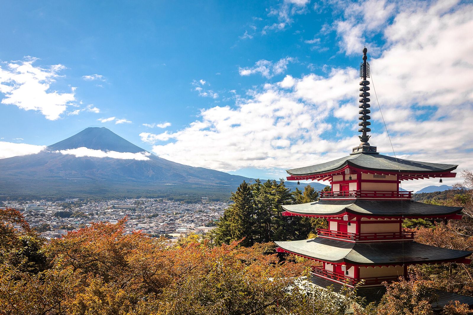 The red five-storey Chureito Pagoda among autumn trees, with Mount Fuji and the town of Fujiyoshida behind