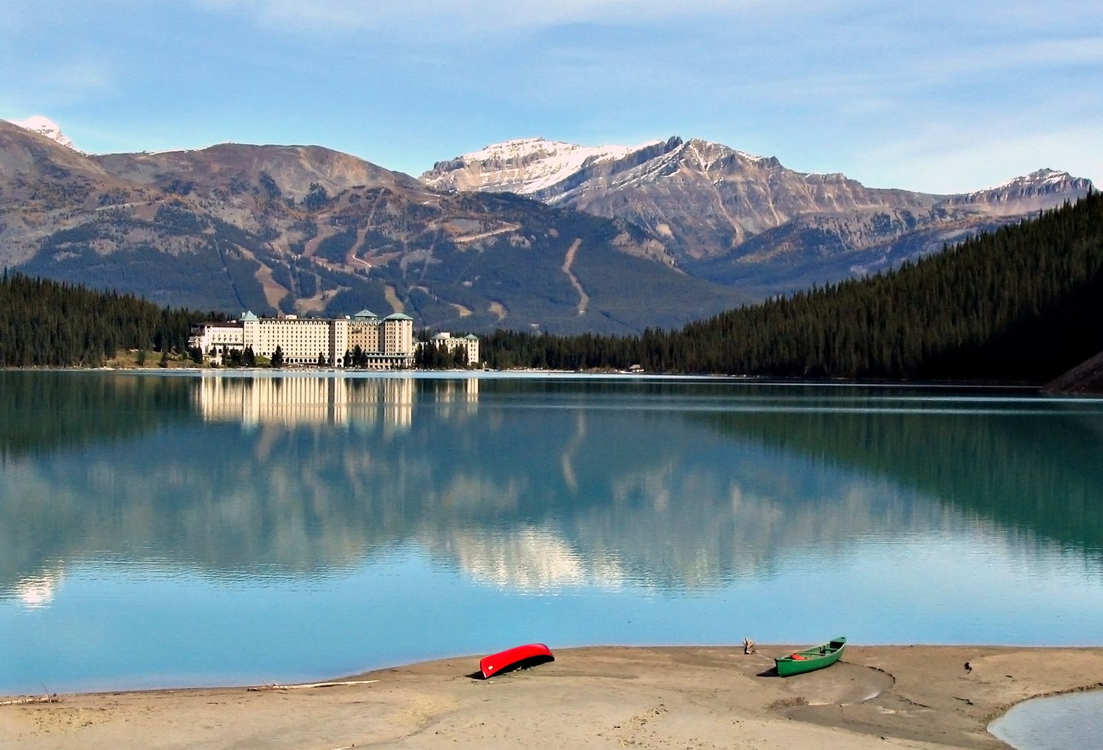 The Fairmont Château Lake Louise reflected in the turquoise water of Lake Louise, with mountains behind