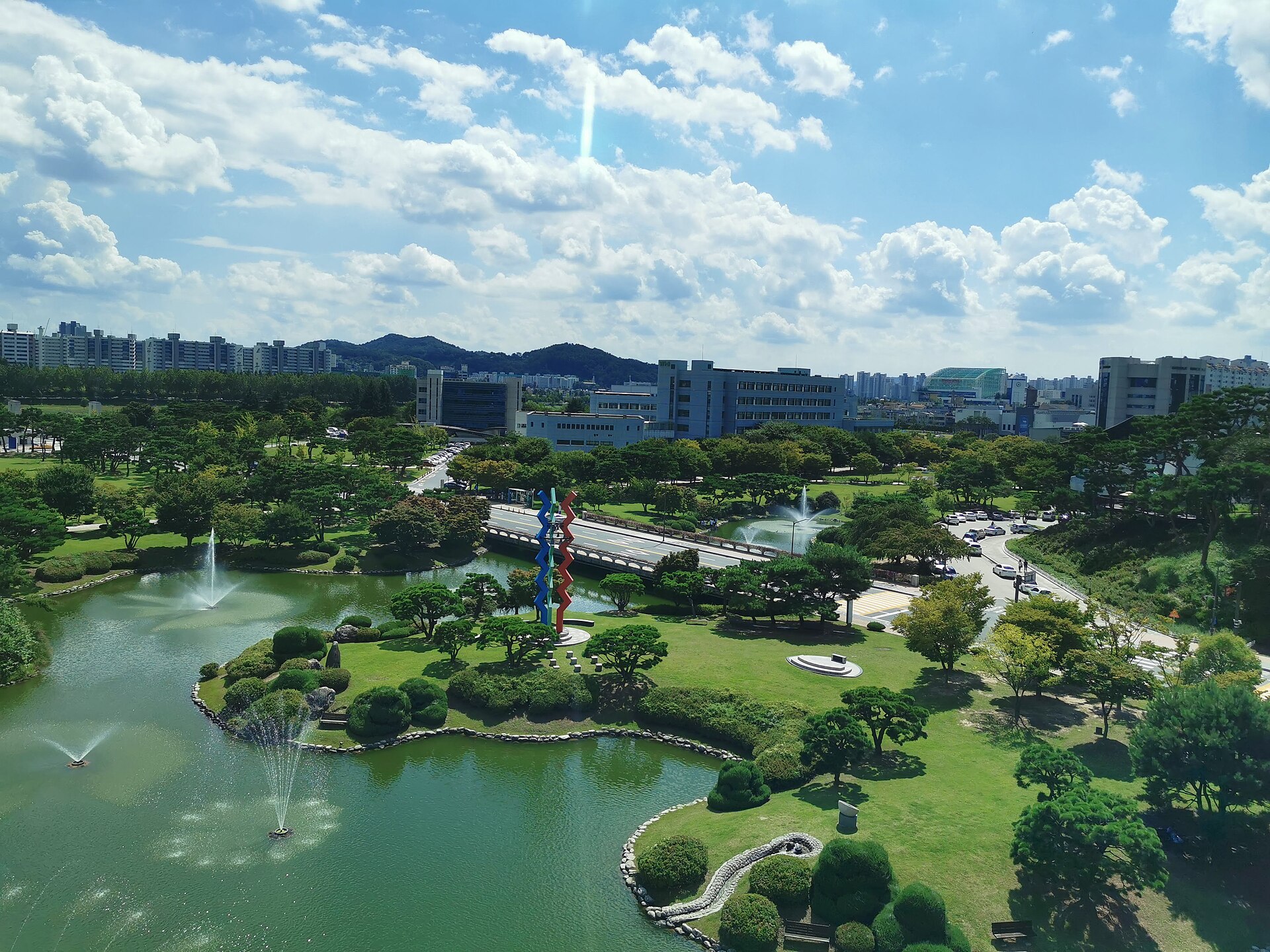 The fountain pond and gardens of the KAIST campus in Daejeon, with the city beyond