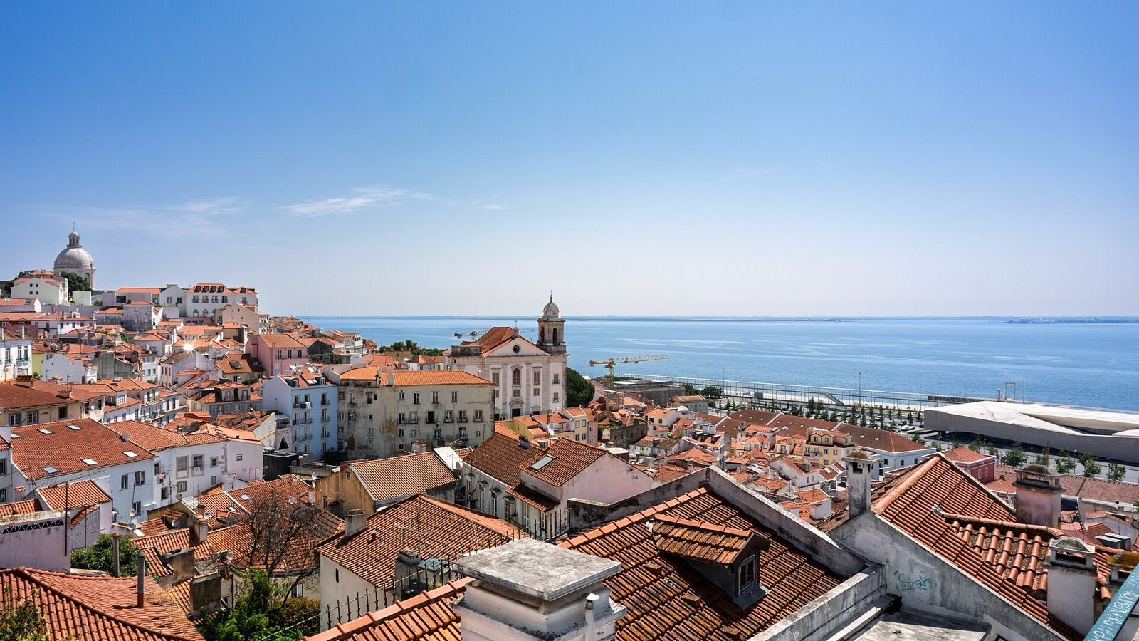 Terracotta rooftops of Alfama sloping down to the Tagus river in Lisbon