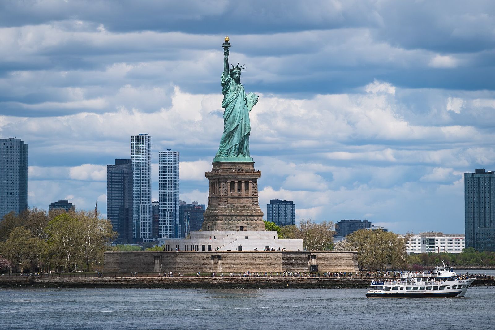 The Statue of Liberty on Liberty Island with a sightseeing boat passing in New York Harbor