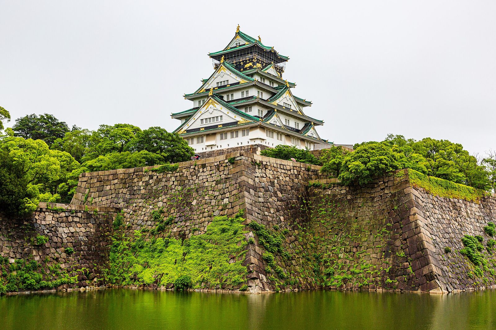 The white and green keep of Osaka Castle rising above massive stone walls and the moat