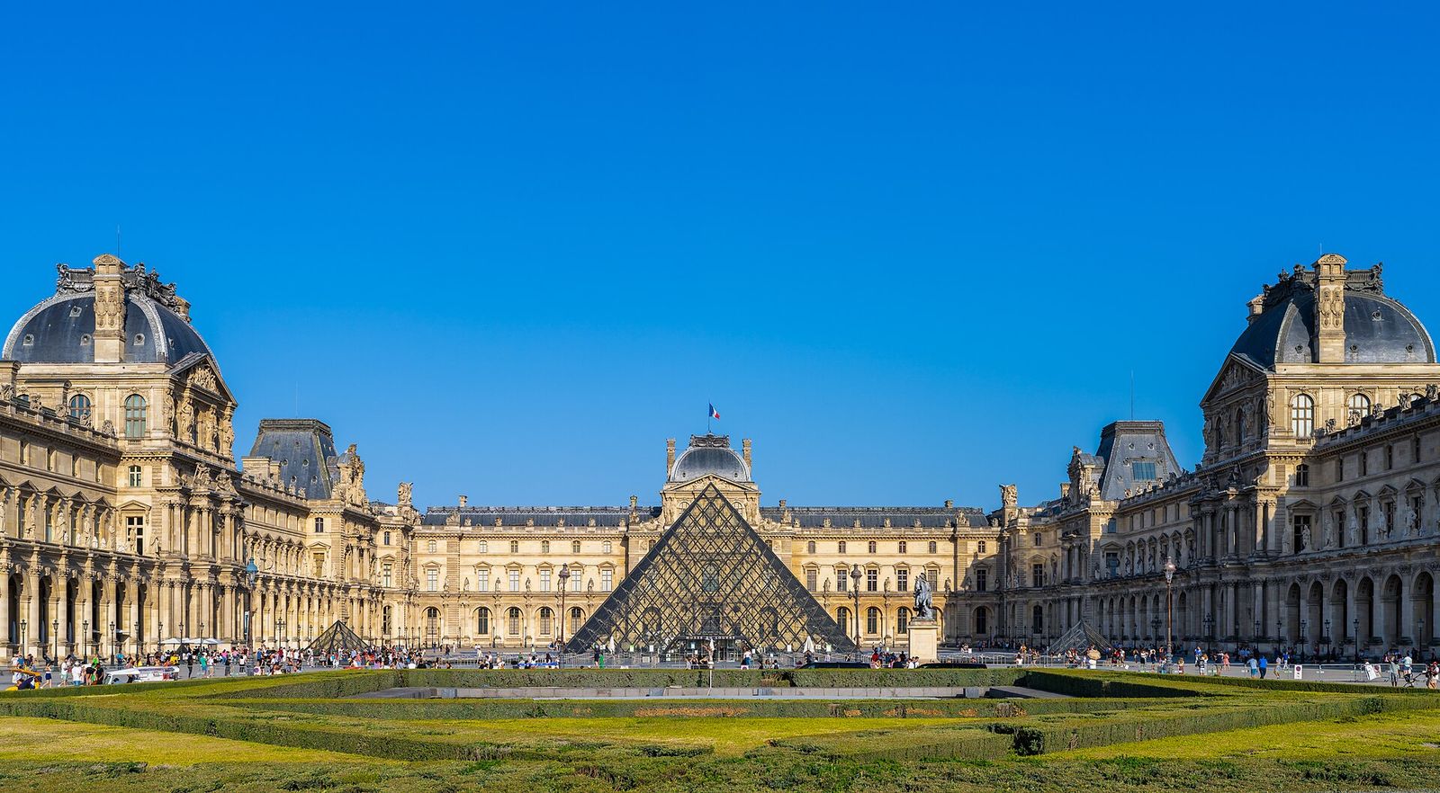 The glass pyramid and the palace wings of the Louvre in Paris under a blue sky