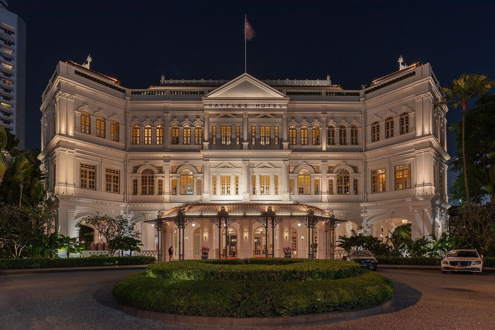The white colonial façade of Raffles Hotel on Beach Road, Singapore, lit up at dusk