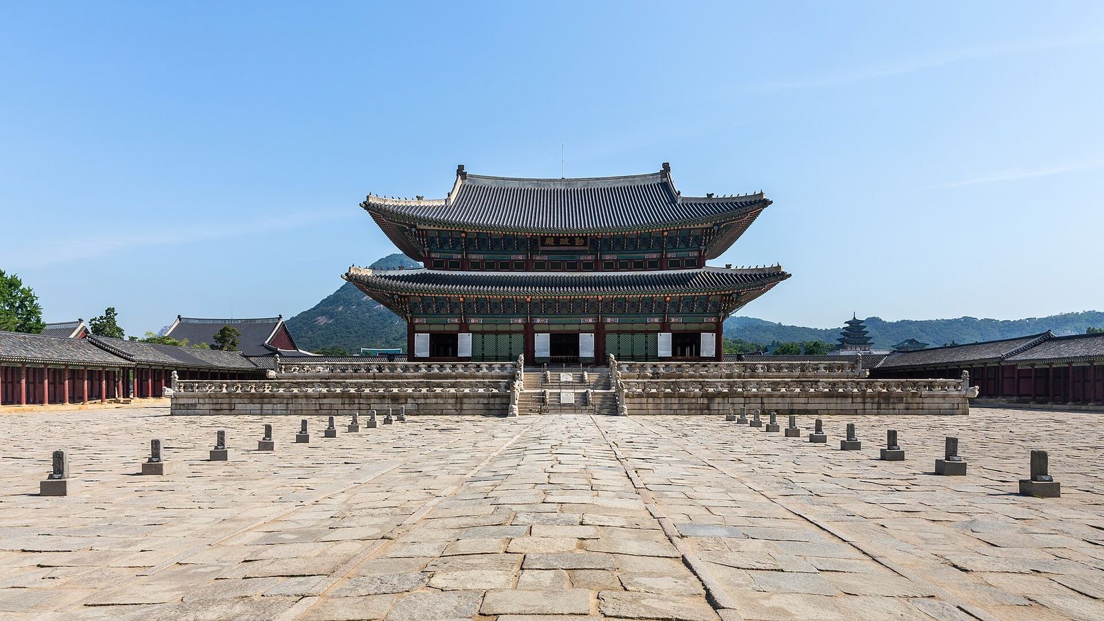 Geunjeongjeon, the two-storey throne hall of Gyeongbokgung Palace, across its stone courtyard with mountains behind