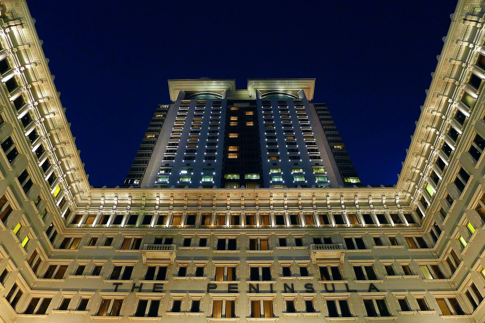 The Peninsula Hong Kong lit up at night, its original wings framing the tower added in the 1990s