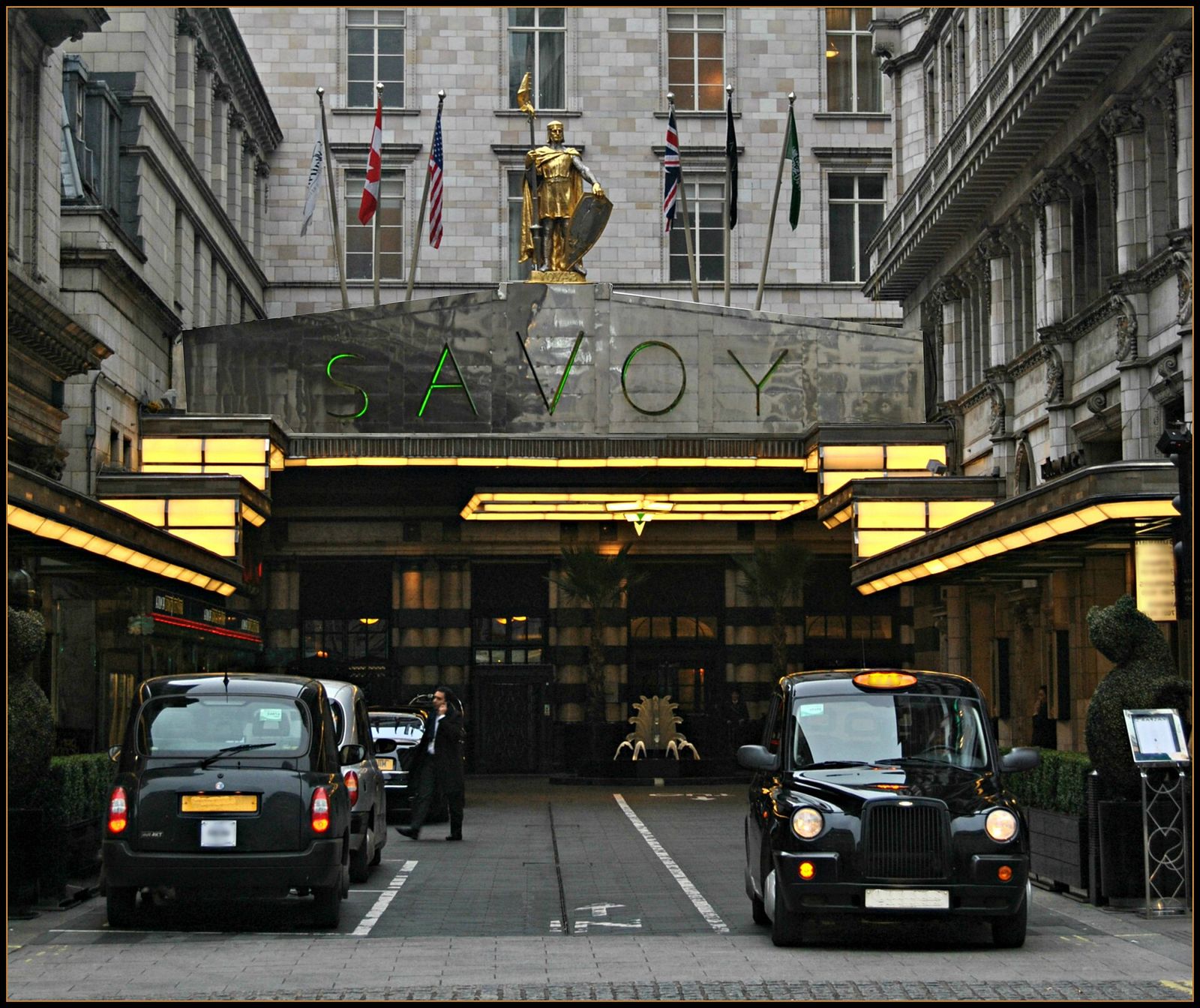 Savoy Court off the Strand, with the hotel's steel canopy, gilded knight statue and black taxis at the entrance