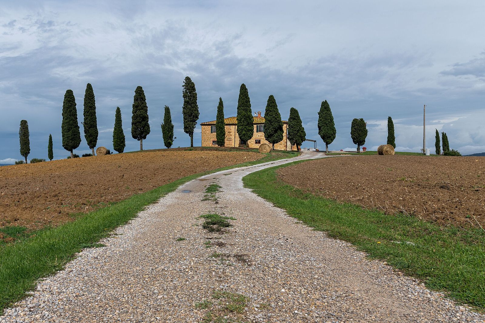 A gravel track leading up to a stone farmhouse ringed by cypress trees in Tuscany's Val d'Orcia