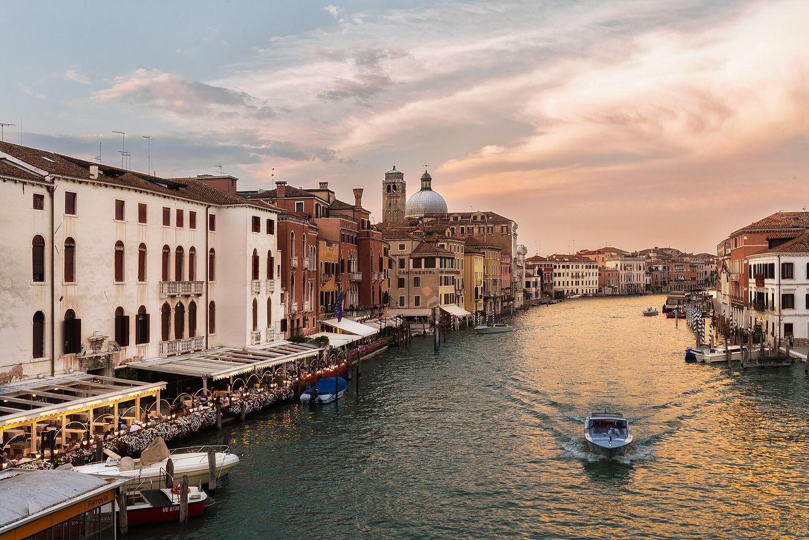 The Grand Canal in Venice at sunset, lined with palaces, canal-side restaurants and moored boats