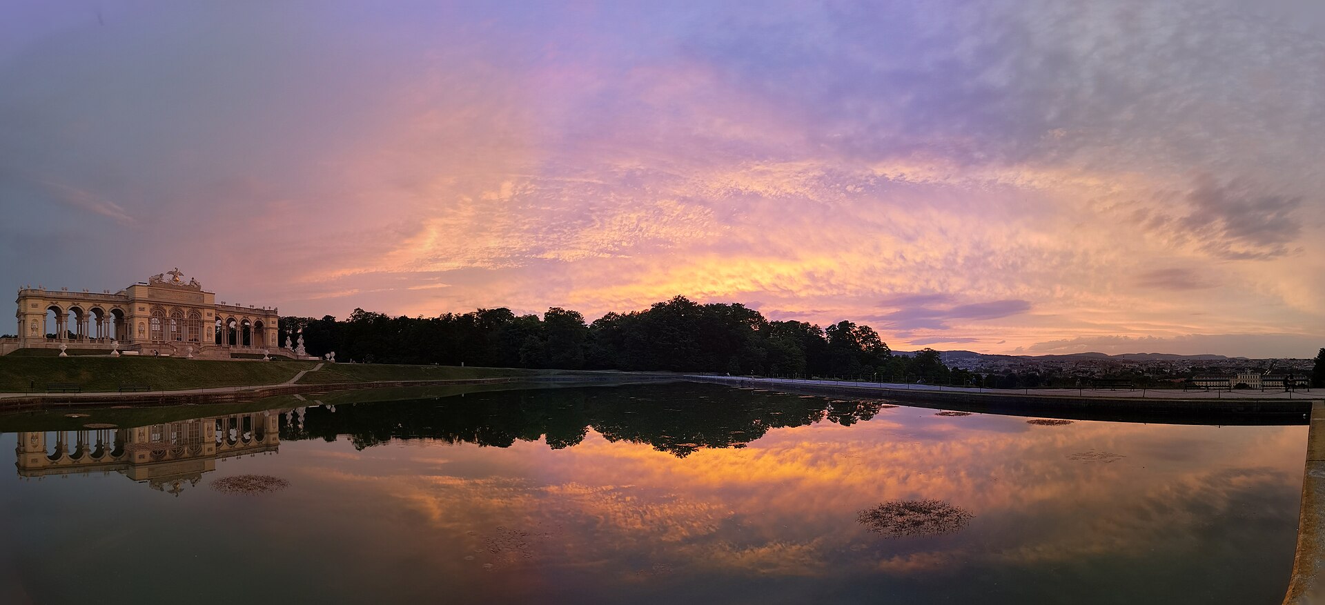 The Gloriette reflected in the pond on the hill above Schönbrunn Palace at sunset, with Vienna in the distance