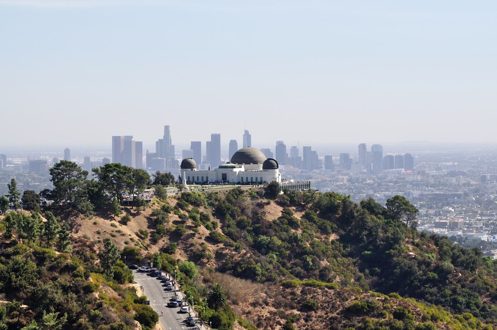 Griffith Observatory on a hilltop in Griffith Park with the towers of downtown Los Angeles in the hazy distance