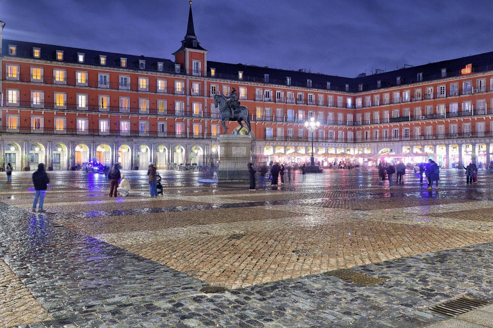 Plaza Mayor in Madrid at dusk, with its arcaded red façades and the equestrian statue of Philip III