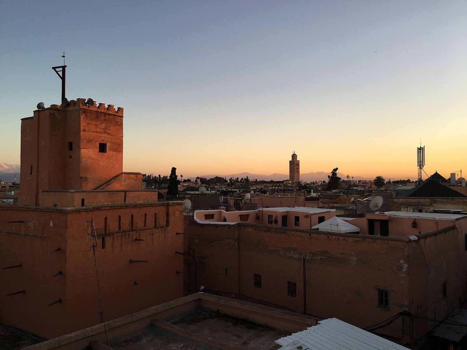 Medina rooftops in Marrakech at sunset, with a minaret and the Atlas Mountains on the horizon