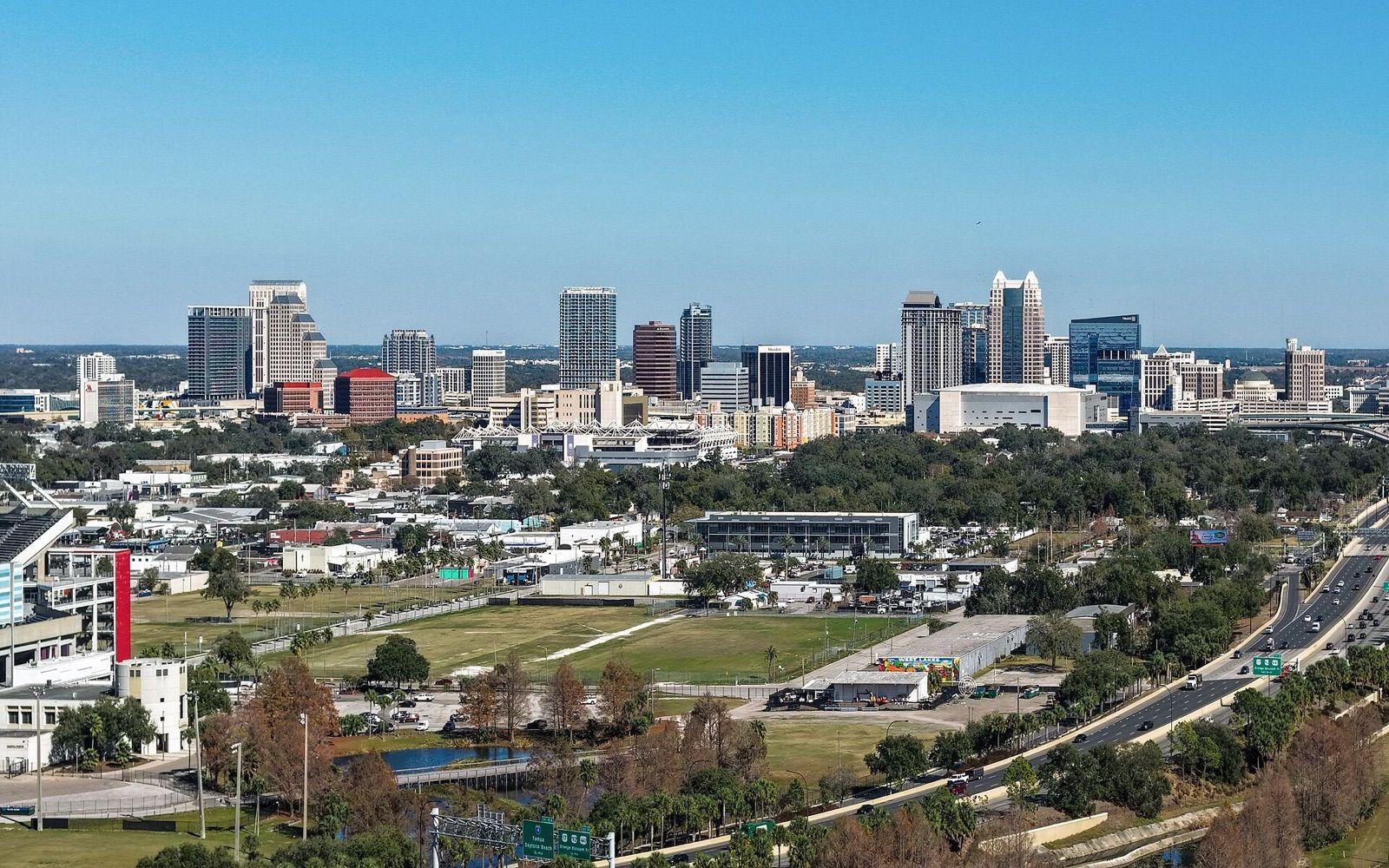 The downtown Orlando skyline above low-rise neighbourhoods and a highway on a sunny day