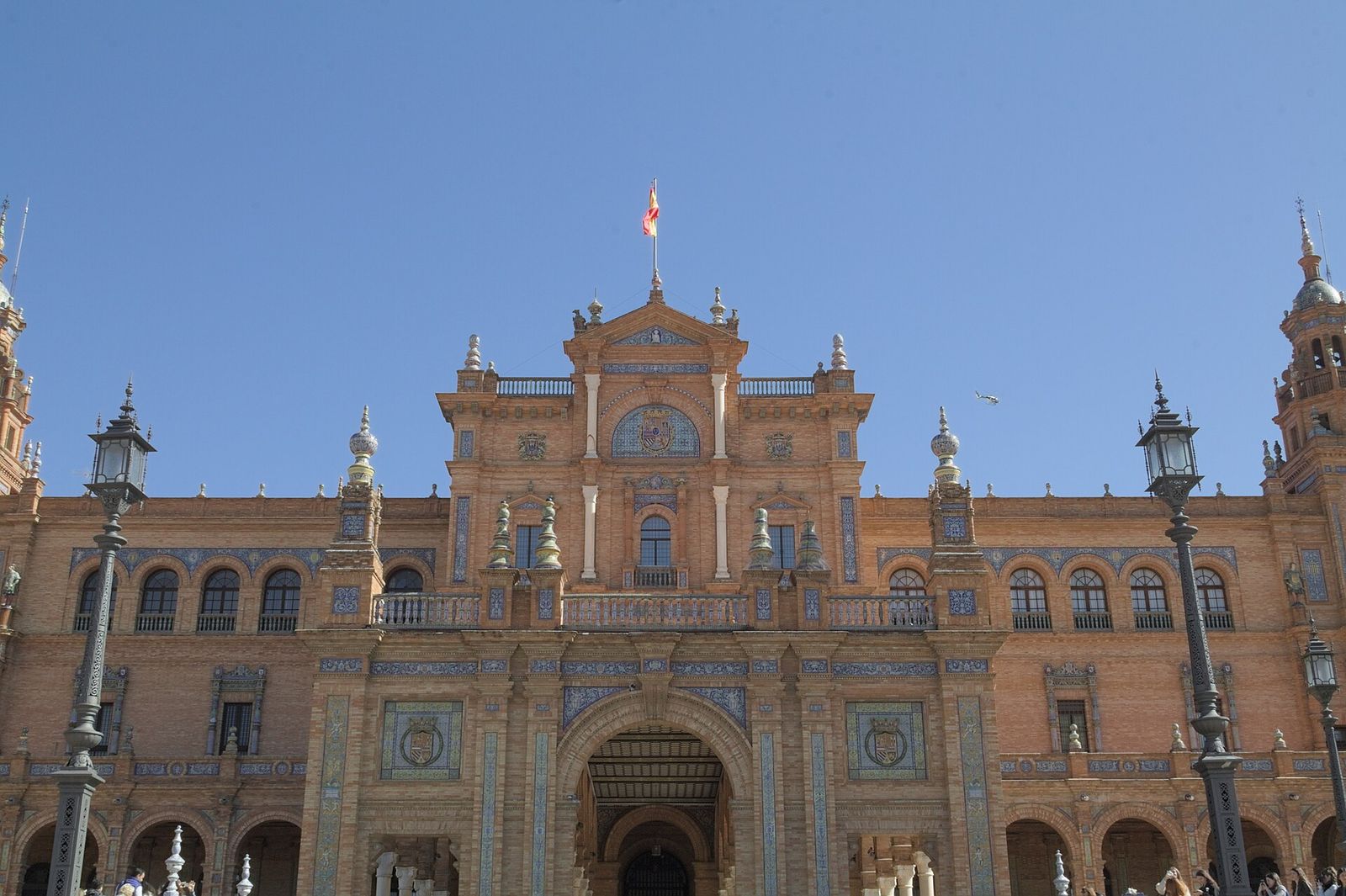 The central building of the Plaza de España in Seville, with brick arches, painted tiles and towers under a blue sky